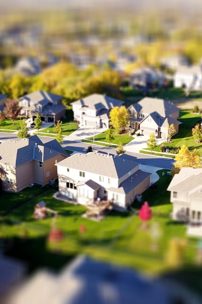 Tilt-shift aerial photo of a suburban neighborhood with green lawns and roads.