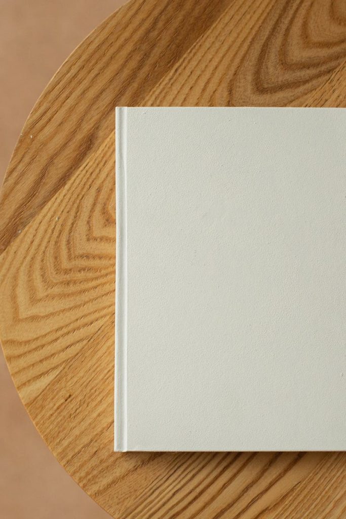 A minimalist white book rests on a textured wooden table, offering ample copy space.